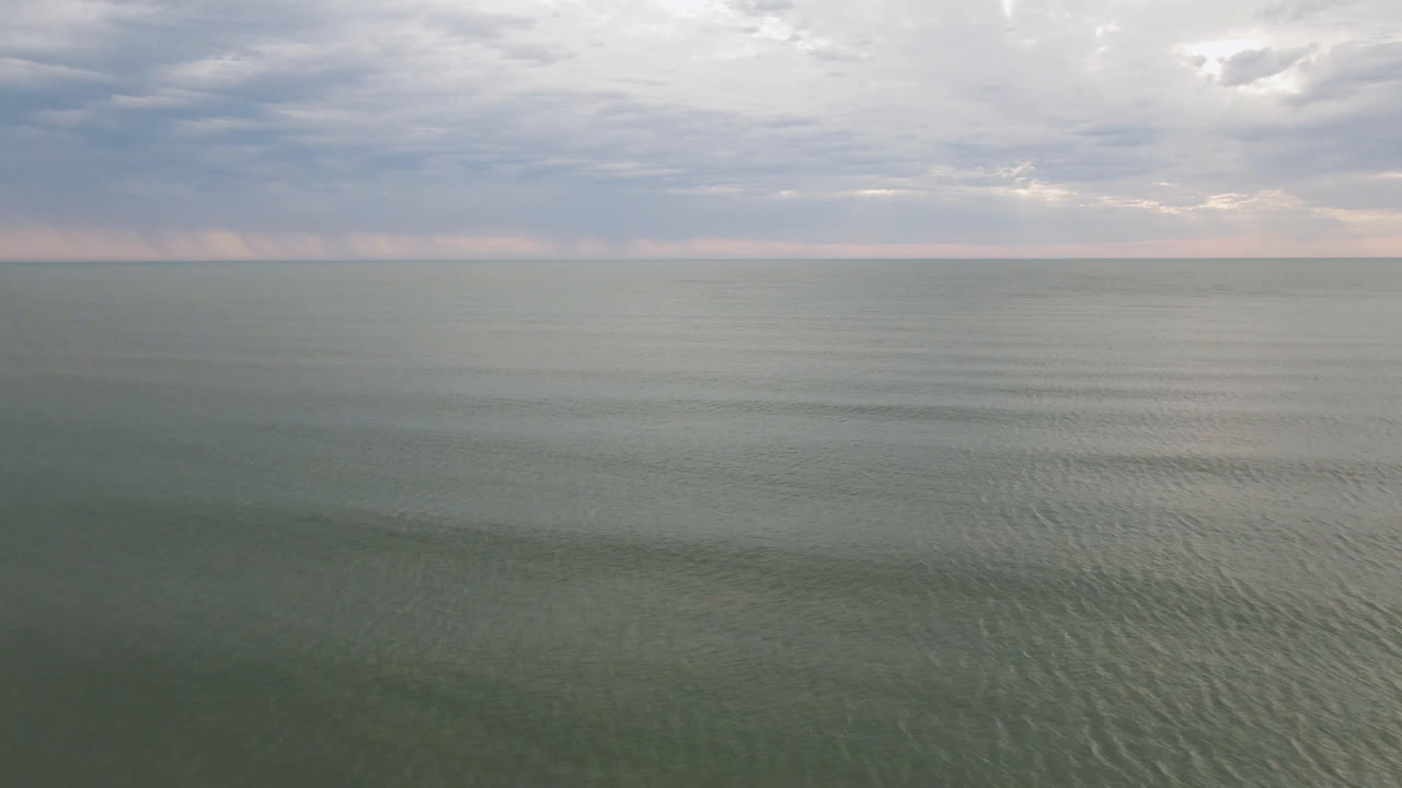Calm San Felipe coastal water fills the foreground, with faint ripples leading to a straight horizon and a layered cloudy sky, no visible people.