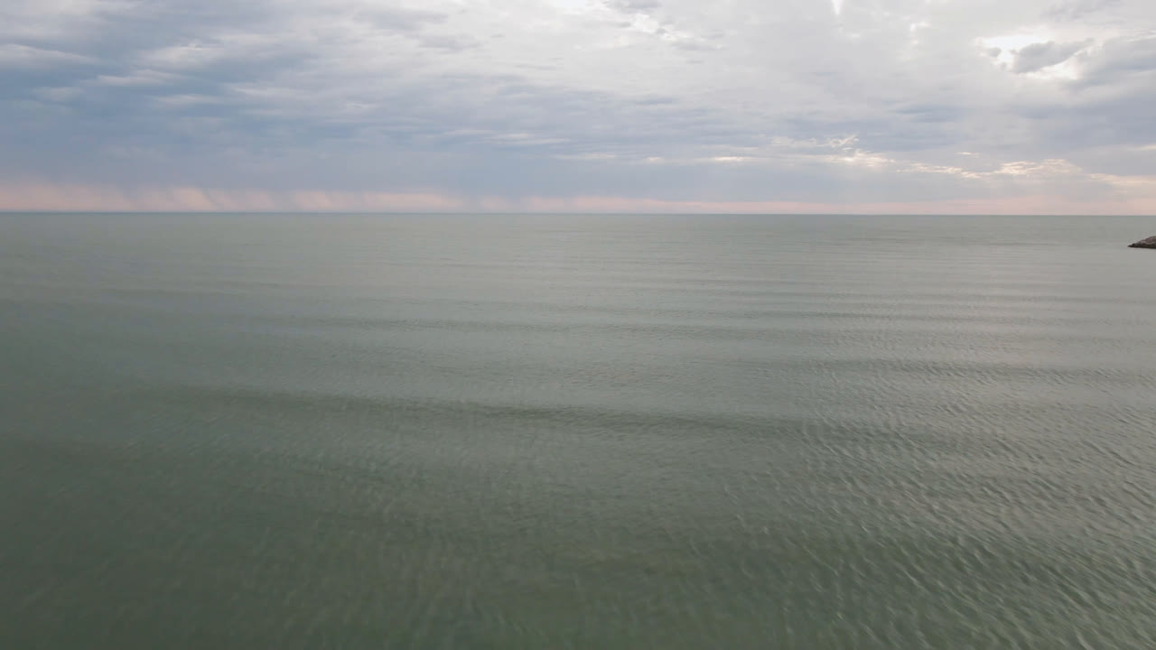 San Felipe ocean fills the frame with faint ripples, a flat distant horizon, a tiny dark boat shape, and no visible people.