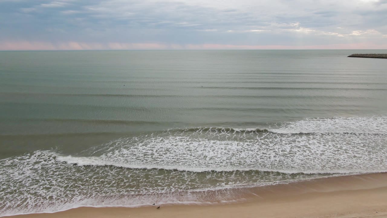 San Felipe BC, Mexico shoreline with thin parallel swells offshore, foamy water spreading toward the beach, and a very small dark figure near the lower edge of the surf.
