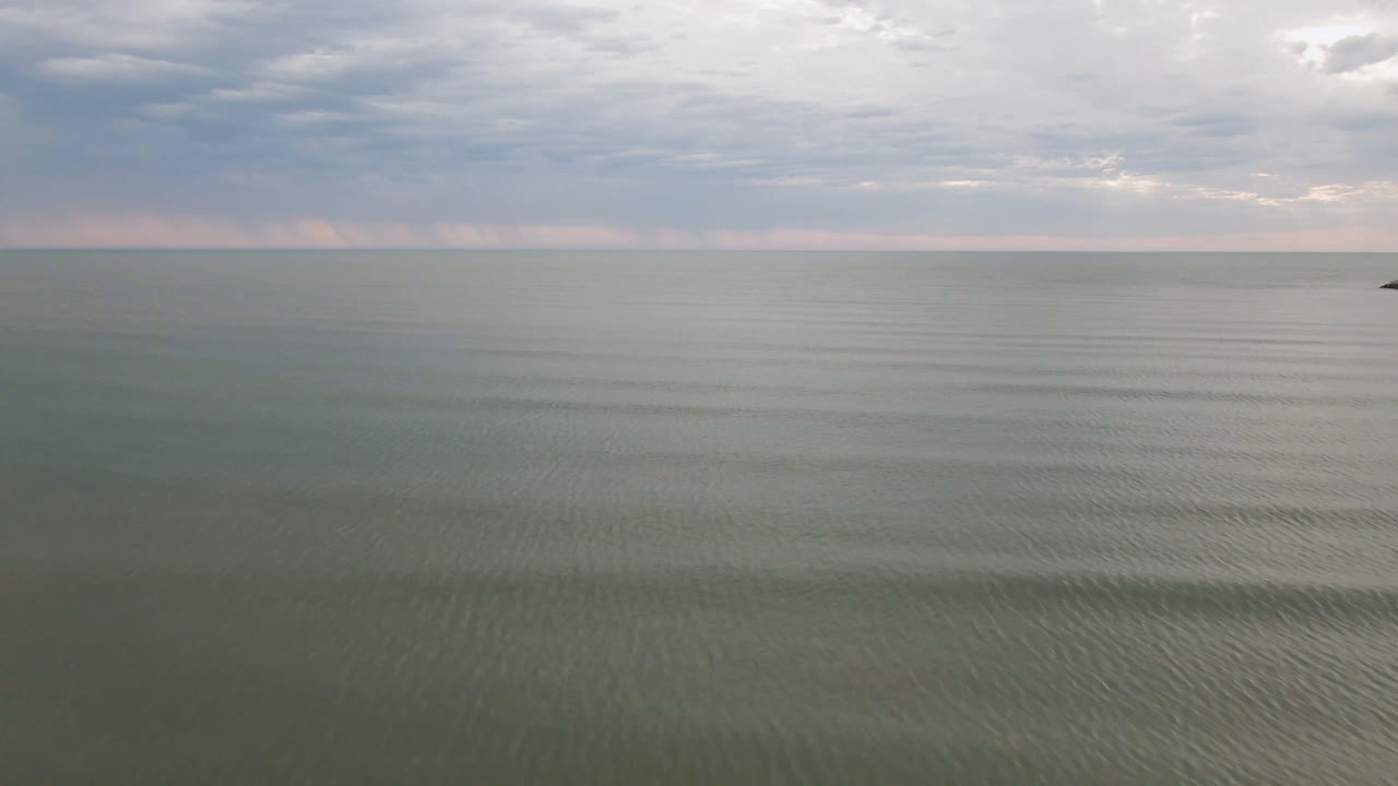 Calm sea beneath overcast clouds with a small dark mark near the right horizon.