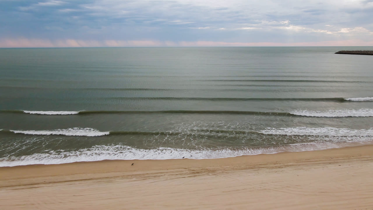 At 0:00, San Felipe beach appears from an elevated view with empty sand, parallel surf lines, a muted ocean horizon, soft clouds, and no visible people.