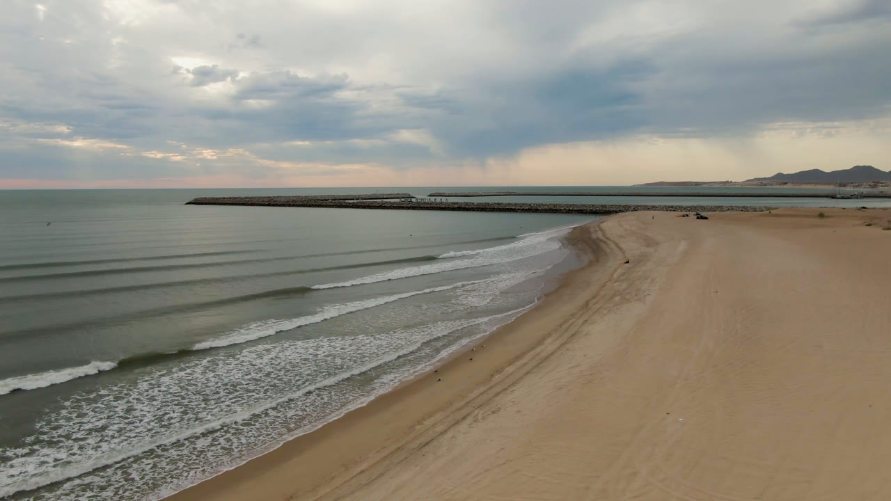 Aerial view in San Felipe, B.C., Mexico, showing parallel wave lines approaching the beach, with the pier stretching across the far water and no visible people.