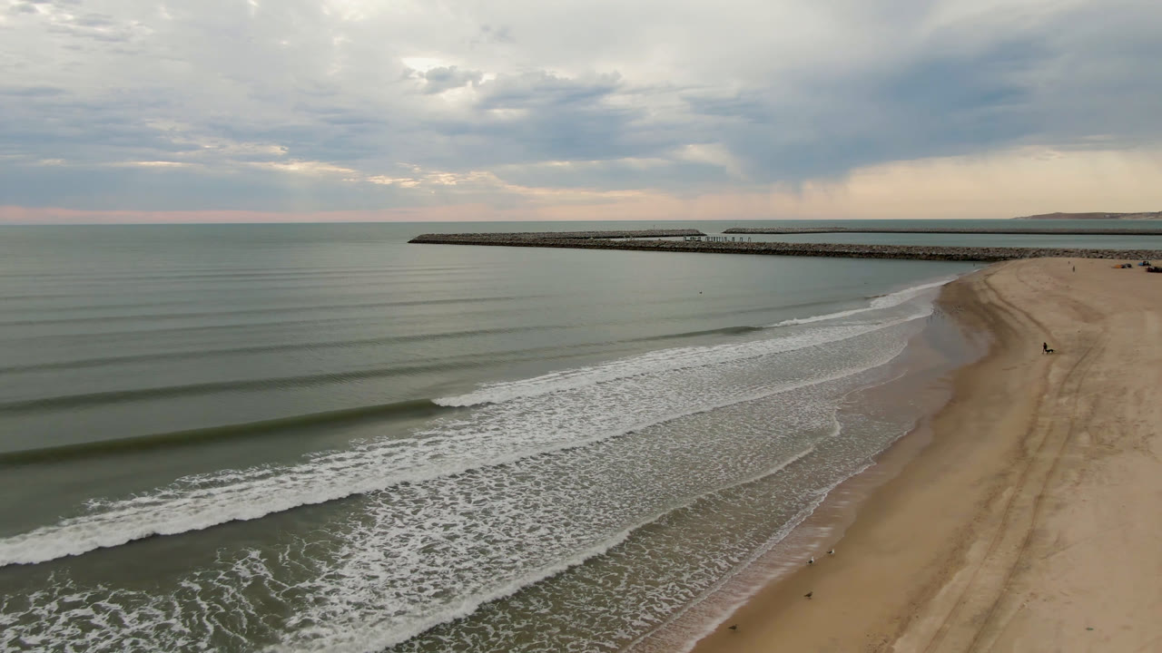 Aerial shoreline view with repeating waves, sandy beach, and cloudy horizon