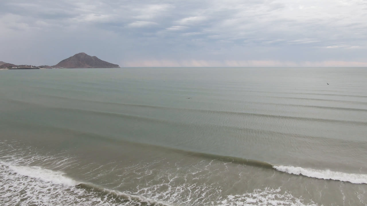 Wide aerial ocean view with foam at lower right and distant rounded land
