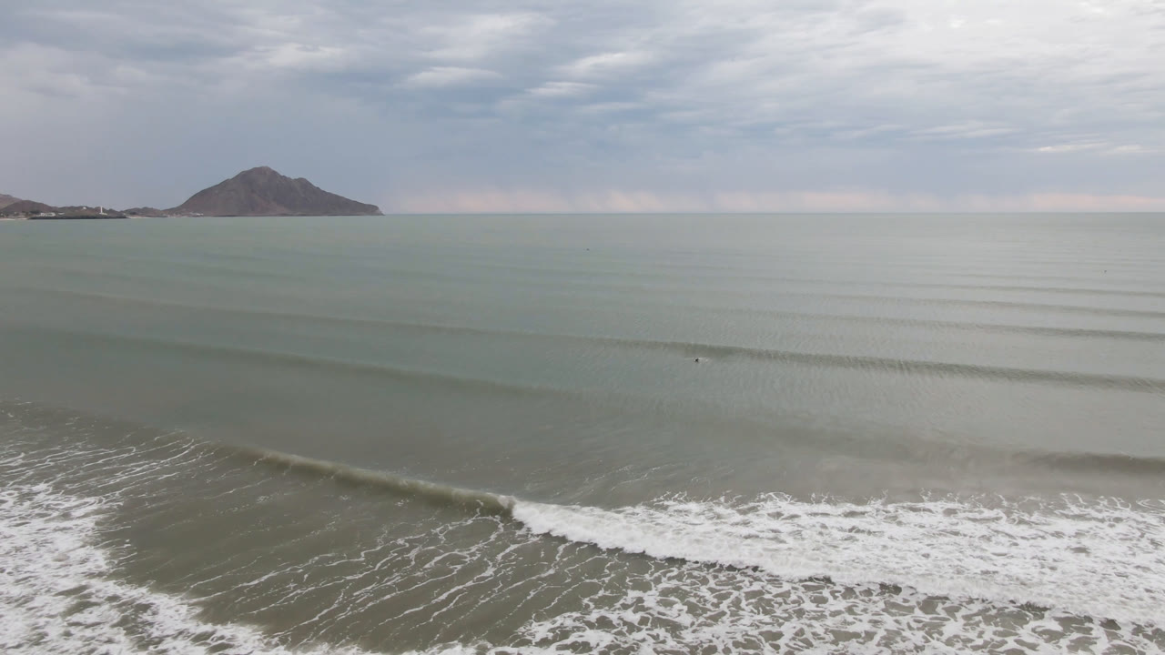 Opening frame over San Felipe, Mexico water with white surf in the foreground, a distant mountain on the horizon, cloudy sky, and no visible people.