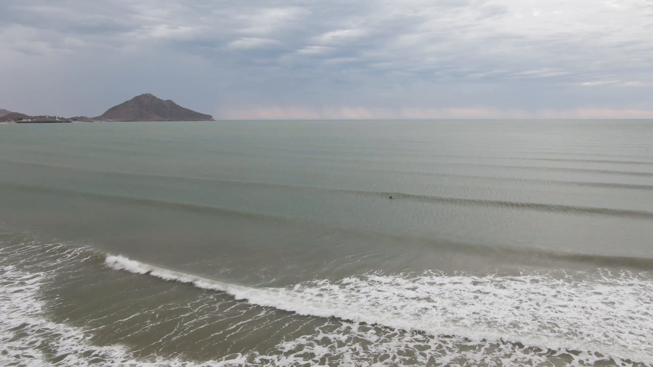 San Felipe, Mexico shoreline view at one second, with a thicker band of white foam in the lower frame, layered green water, distant mountain, and no visible people.