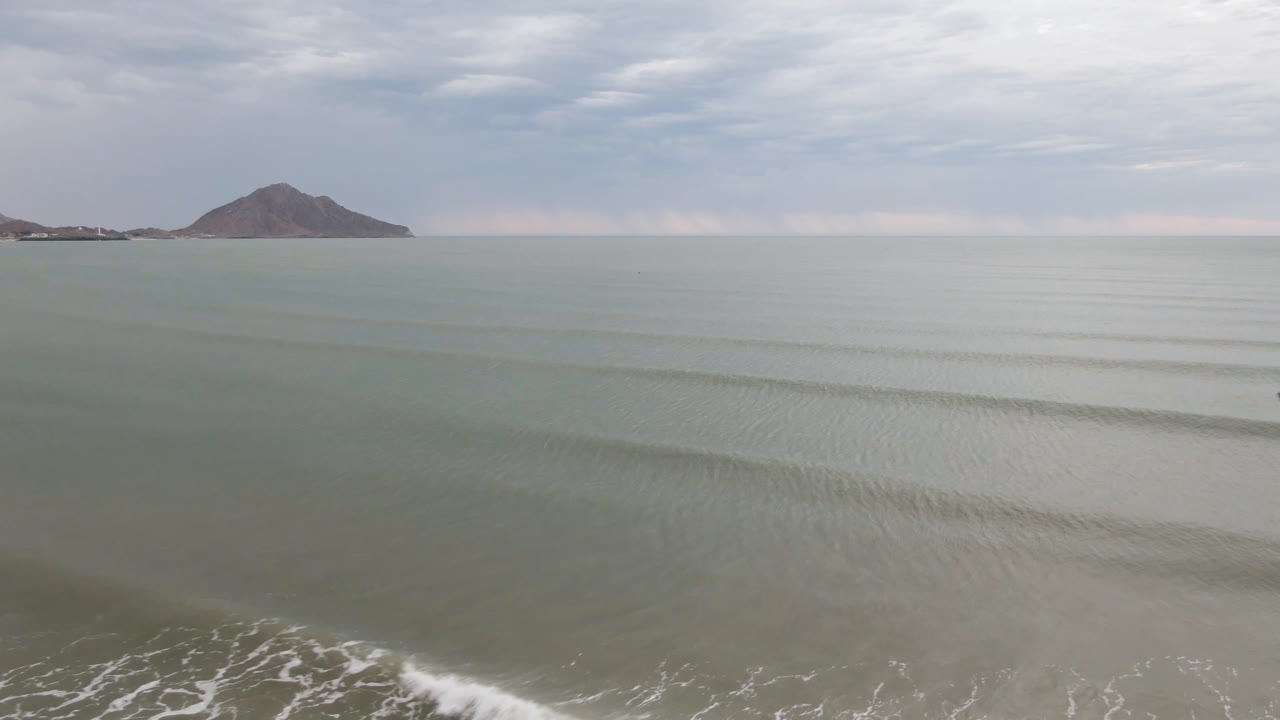Opening frame of San Felipe water with faint surf in the lower left, a distant mountain on the horizon, layered clouds above, and no visible people.