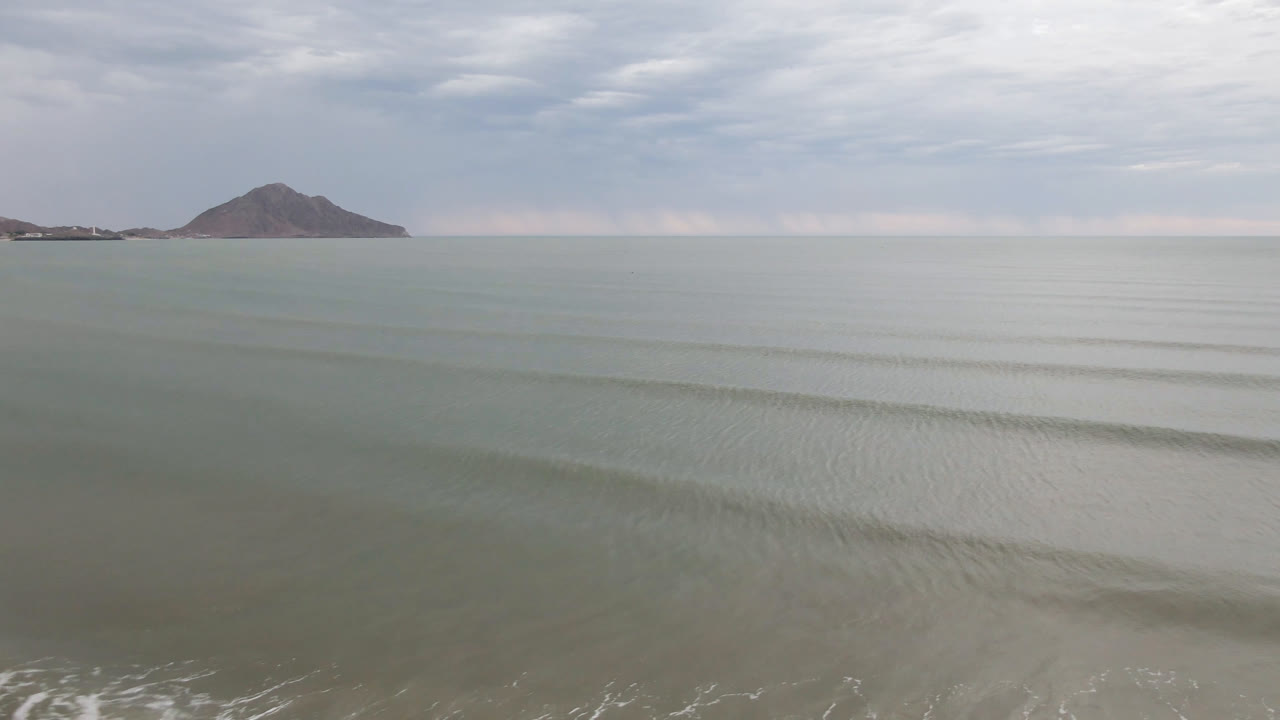 Second frame shows San Felipe's green-gray water spread across the foreground, thin parallel wave bands in the midground, the distant mountain, and no visible people.
