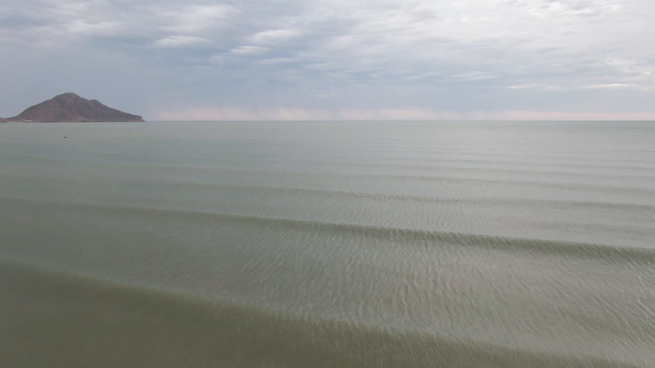 Calm green-gray water in San Felipe BC Mexico stretches toward a small boat near the horizon, with a dark mountain beyond and no visible people.