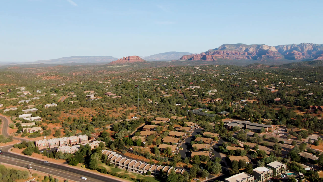 At 0:01, the Sedona aerial holds on curving roads, clusters of low buildings, desert vegetation, distant red rock formations, and no visible people.