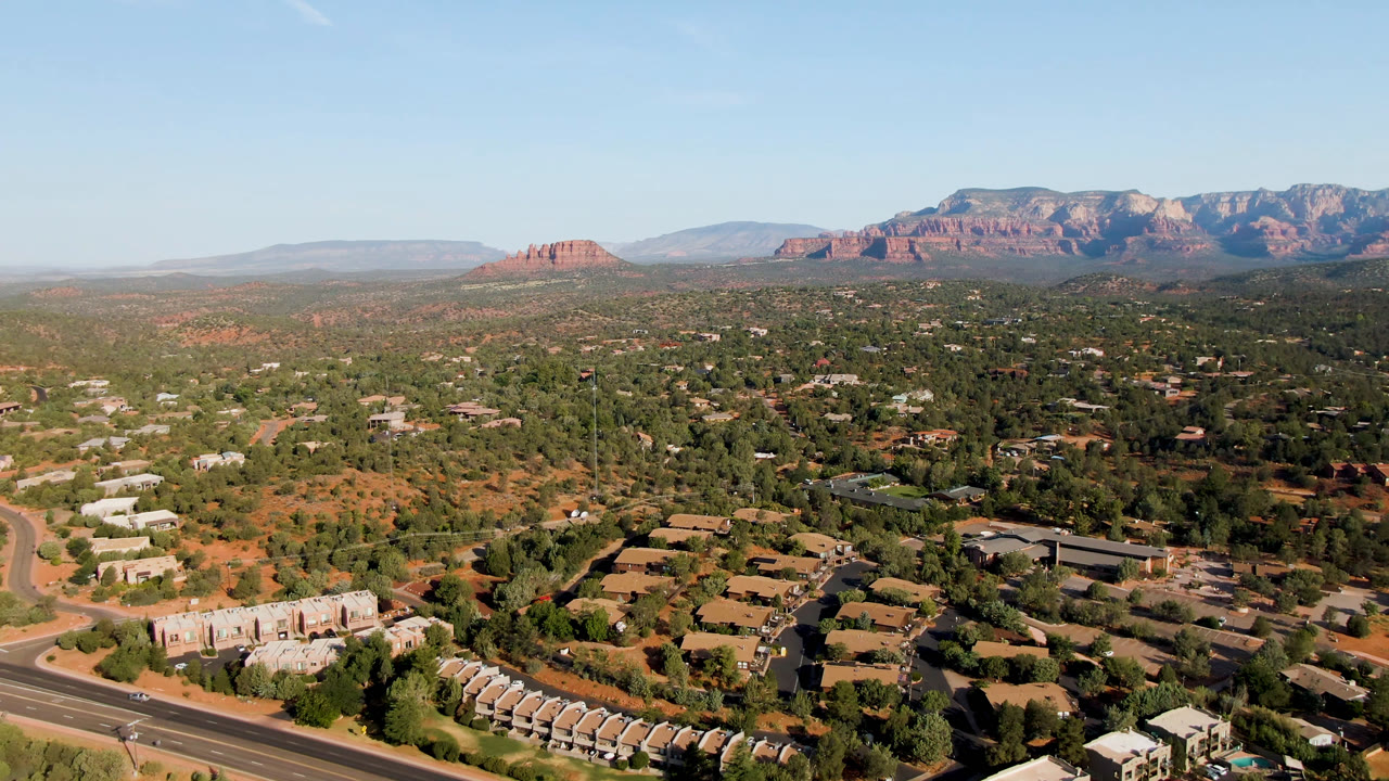 At 0:02, Sedona appears from above with residential blocks, a main road near the lower edge, green tree cover, red earth, distant mesas, and no visible people.