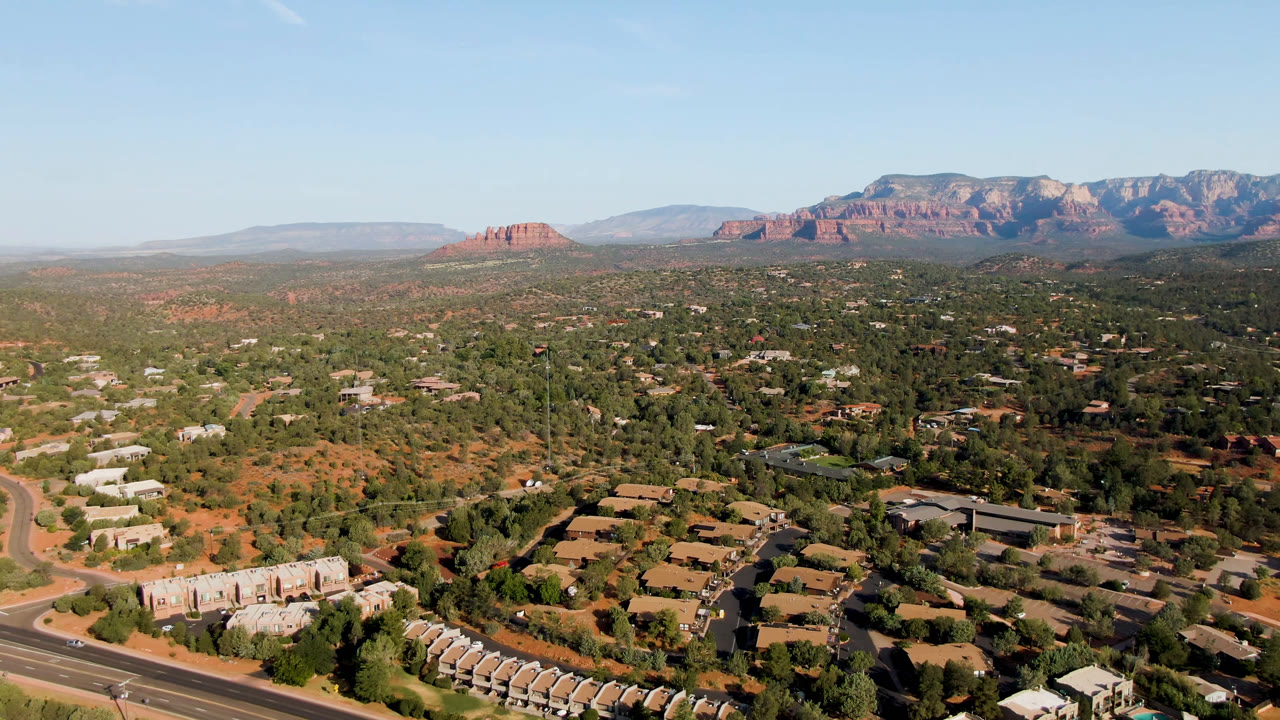 Desert town aerial with road at lower left and red rock ridge in the distance.