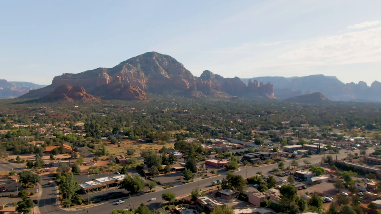Sedona, Arizona aerial frame with the mountain ridge centered higher in the composition, town blocks and desert vegetation below, and no visible people.