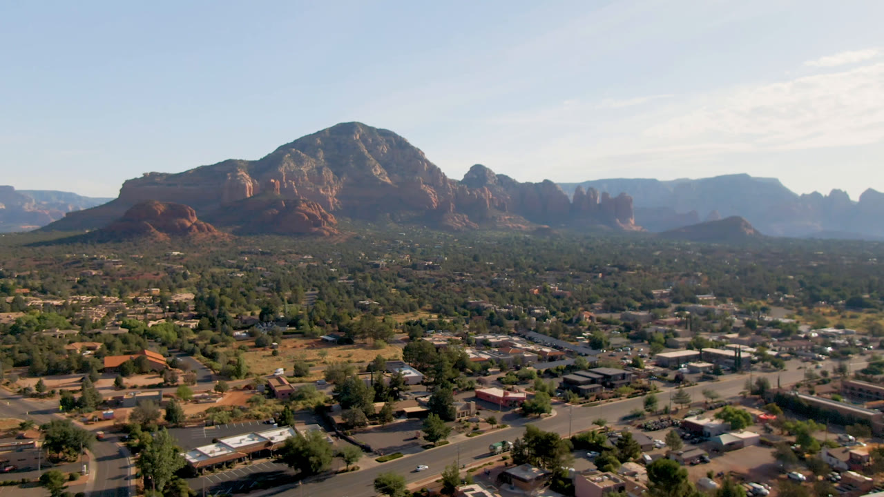 Elevated view across Sedona buildings and trees toward red rock mountains.