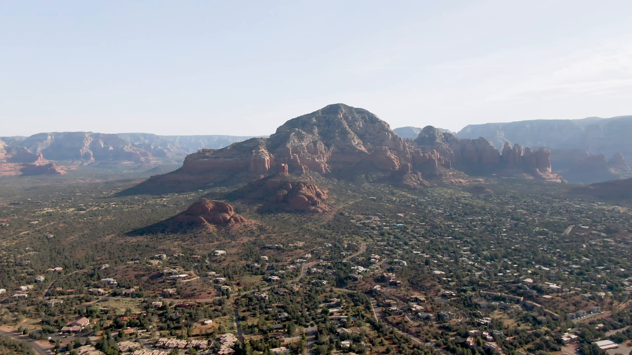 Second frame of Sedona, Arizona with the central red rock mass slightly more prominent over the gridded town foreground, open desert, distant mesas, and no visible people.