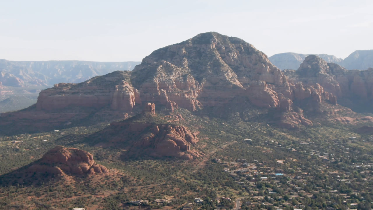 Opening frame of Sedona, Arizona, with red rock formations rising above a green valley and small town structures visible below, no visible people.