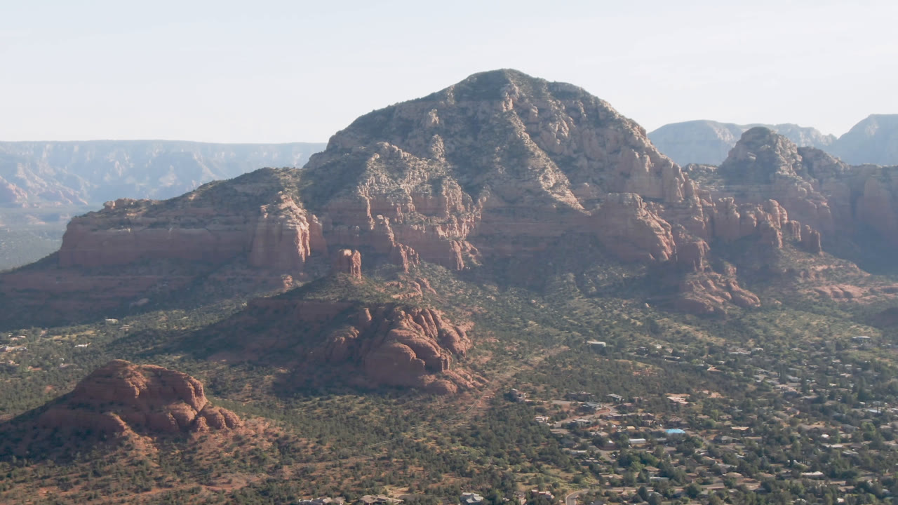 Aerial landscape with red rock buttes, a town, and distant mesas.