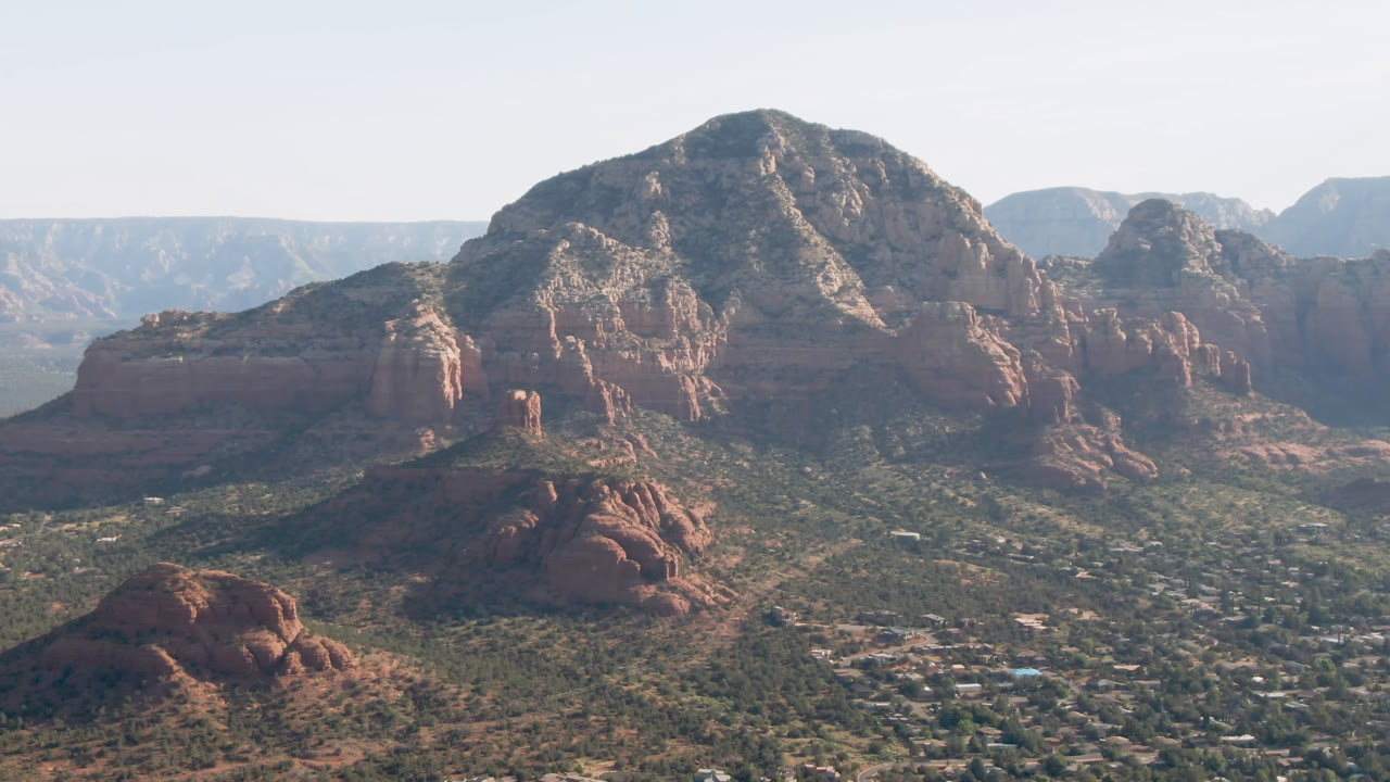 Wide Sedona, Arizona frame with the central mountain mass dominating the upper image and small buildings scattered through the valley floor, no visible people.