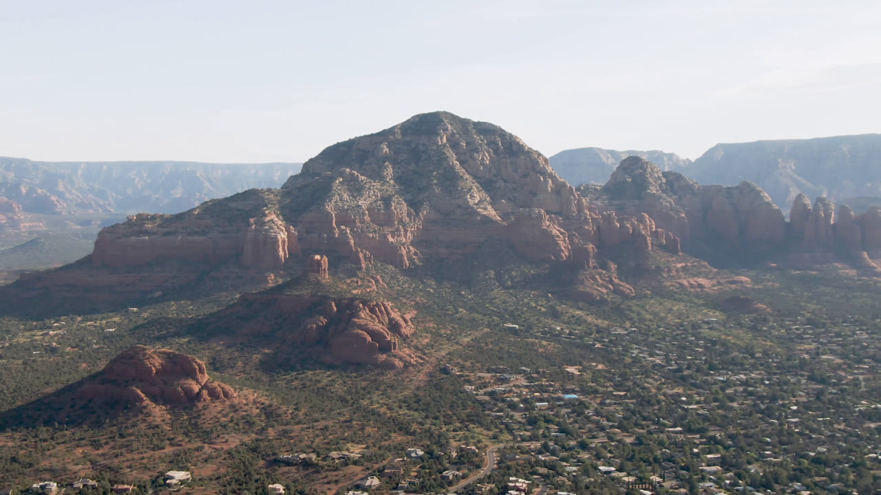 Wide aerial view of red rock mountains above a valley town.