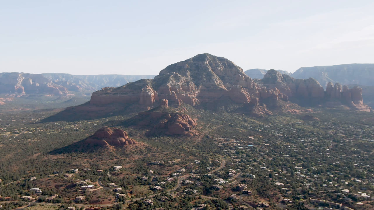 Second frame over Sedona, Arizona, with the central red rock mass more prominent above roads, low buildings, desert vegetation, and no visible people.