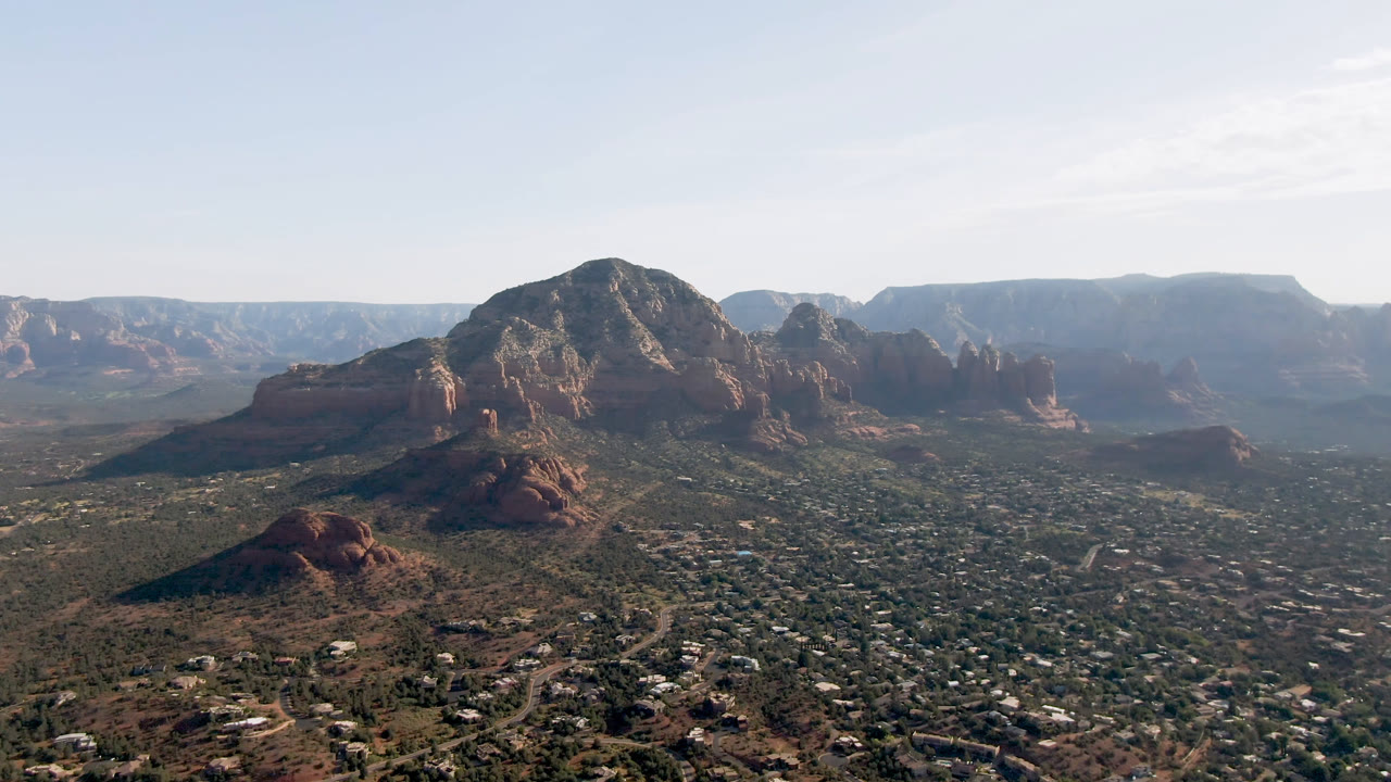 Opening frame of Sedona, Arizona from above, with a broad valley and scattered buildings below red rock formations and no visible people.