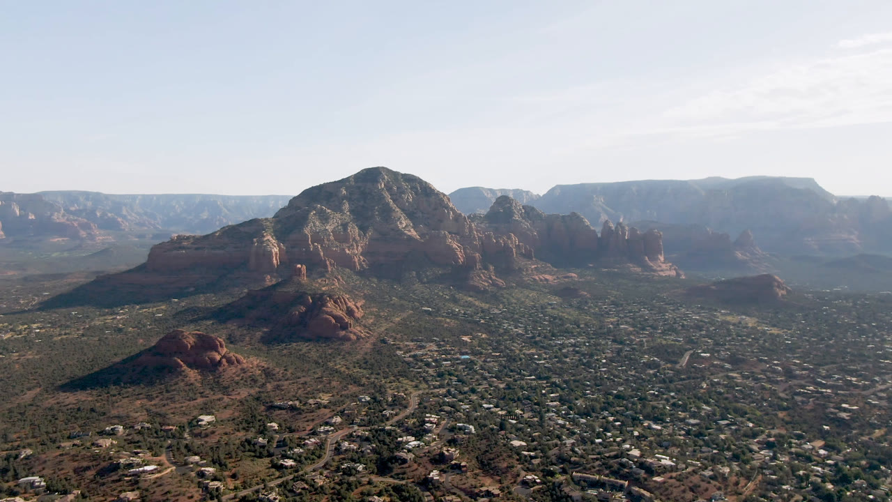 Sedona aerial frame with the central mountain mass slightly more prominent over the valley, red rock buttes to the side, and no visible people.