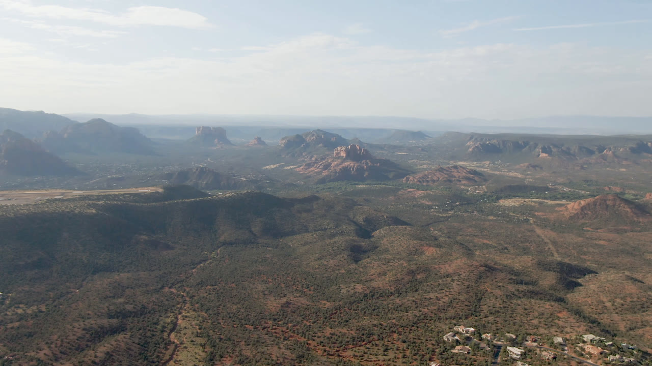 Opening frame of Sedona, Arizona from above, with scrub-covered valley ridges, red rock formations, distant mesas, and no visible people.