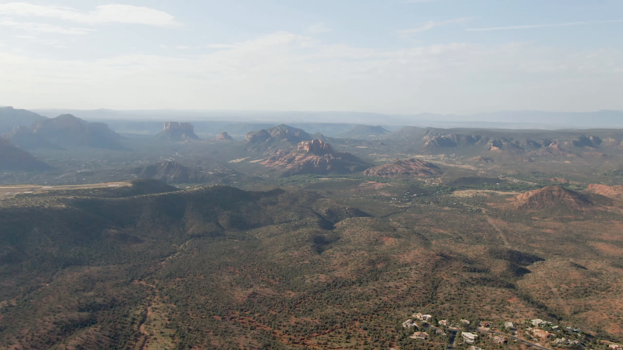 Aerial view of scrubby valley terrain with red rock formations and open sky.