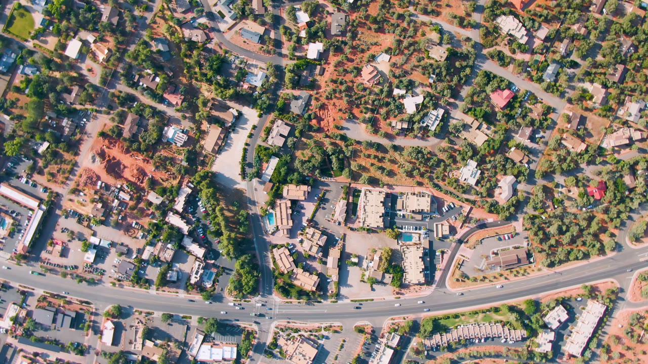 Second overhead frame in Sedona, Arizona with the main road running across the lower frame, homes and small buildings above it, and no visible people.