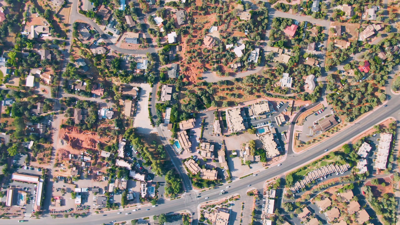 Overhead view of a diagonal road through trees, homes, lots, and red desert ground.