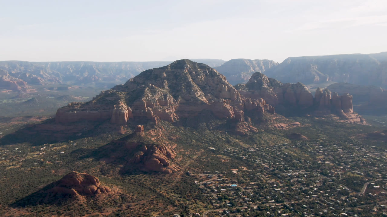 Wide aerial view of red rock formations above a desert city and valley.