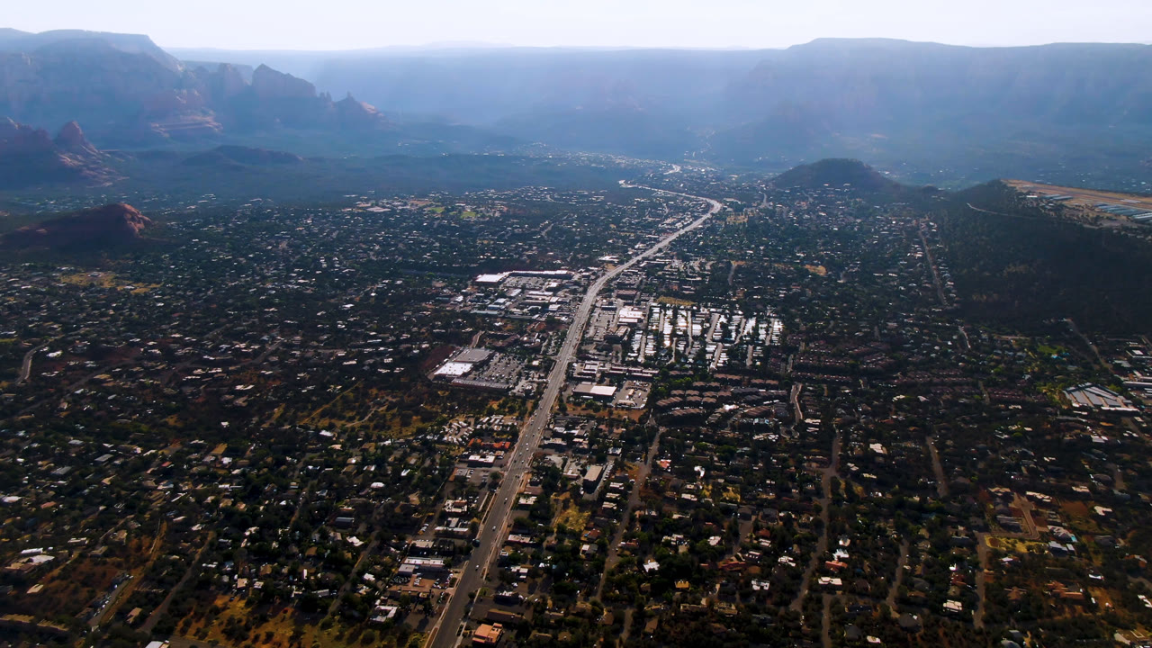 High aerial over Sedona with road, buildings, and mesas.