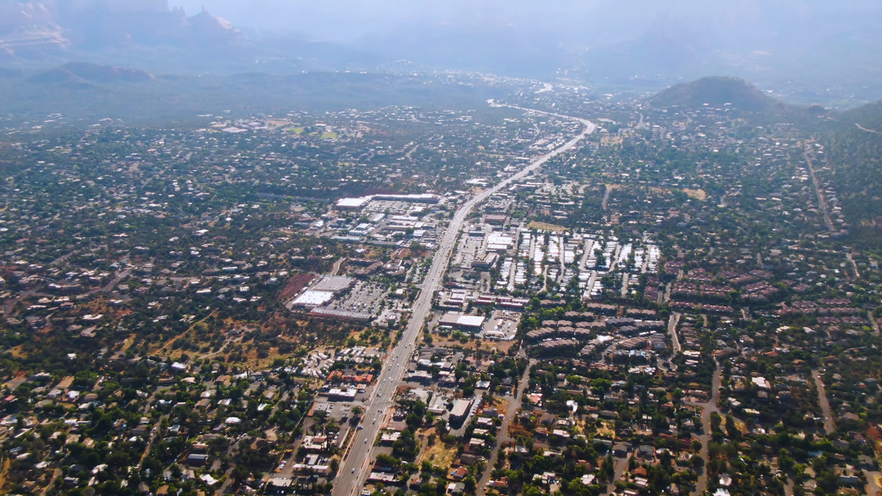 Wide aerial view over a desert town with a main highway and hazy hills.