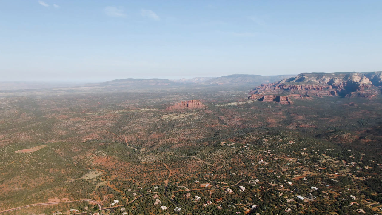 Aerial landscape with open desert, low red buttes, and a large rock bluff.
