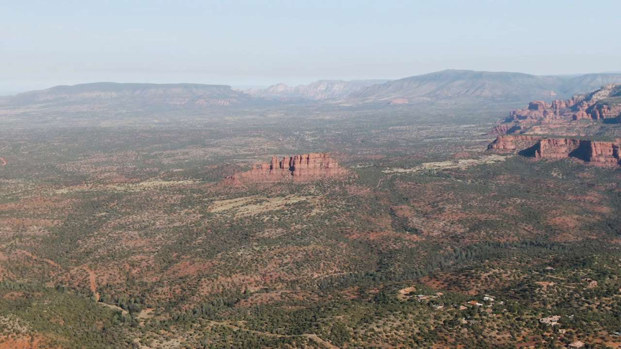 Broad valley landscape with red bluffs, trees, and a hazy mountain background.