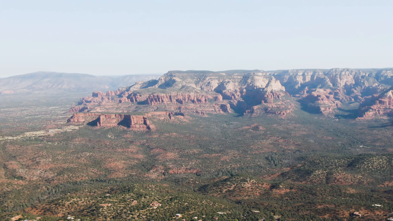 Wide aerial view of red rock bluffs above a scrub-covered valley