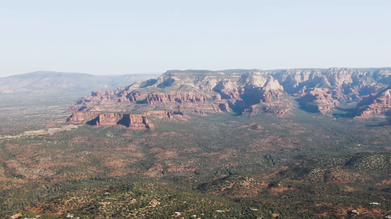 Second frame over Sedona, Arizona showing the red and pale cliff band across the center, low desert vegetation in the foreground, distant ridges, and no visible people.