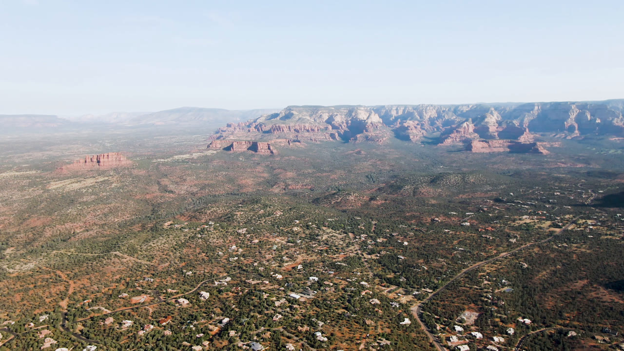 Wide aerial view over desert valley homes and distant red rock mountains.