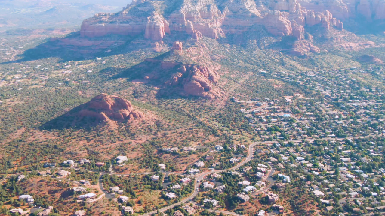 Aerial view of red rock buttes, desert vegetation, roads, and scattered buildings.