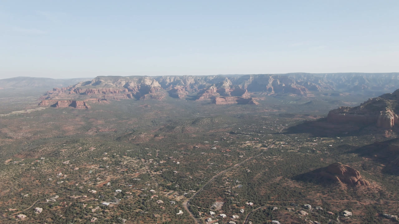 Wide aerial view of a desert valley with red rock cliffs and scattered buildings.