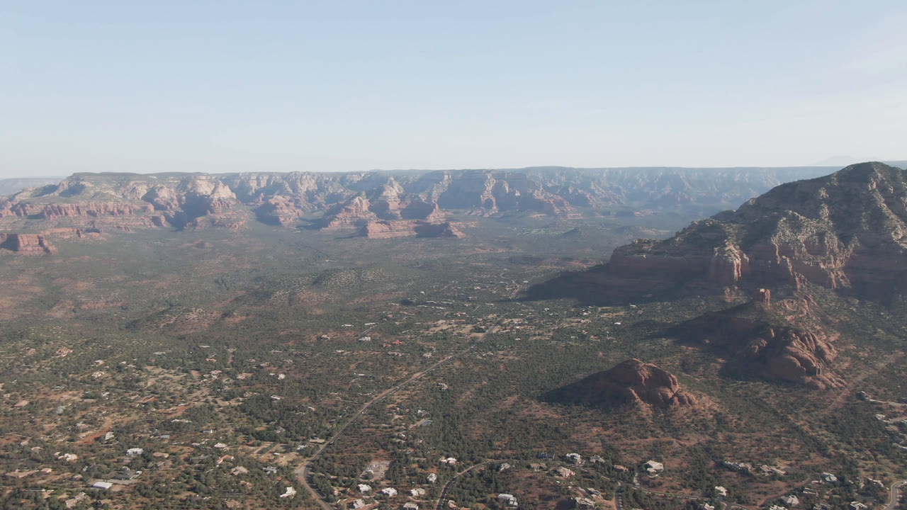 High aerial view over Sedona valley with scattered buildings and layered red rock background.