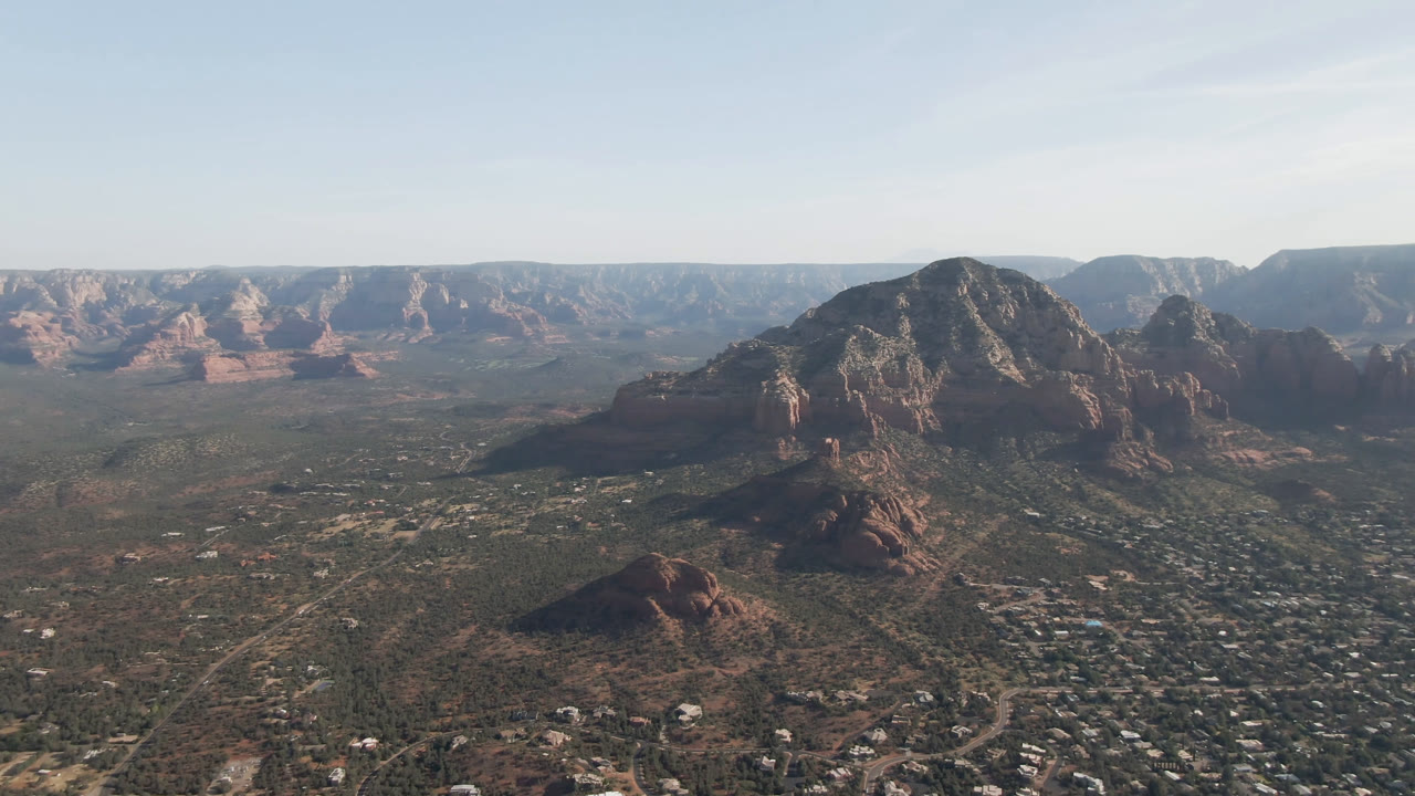 Wide aerial view of red rock mountains above a desert town and valley.
