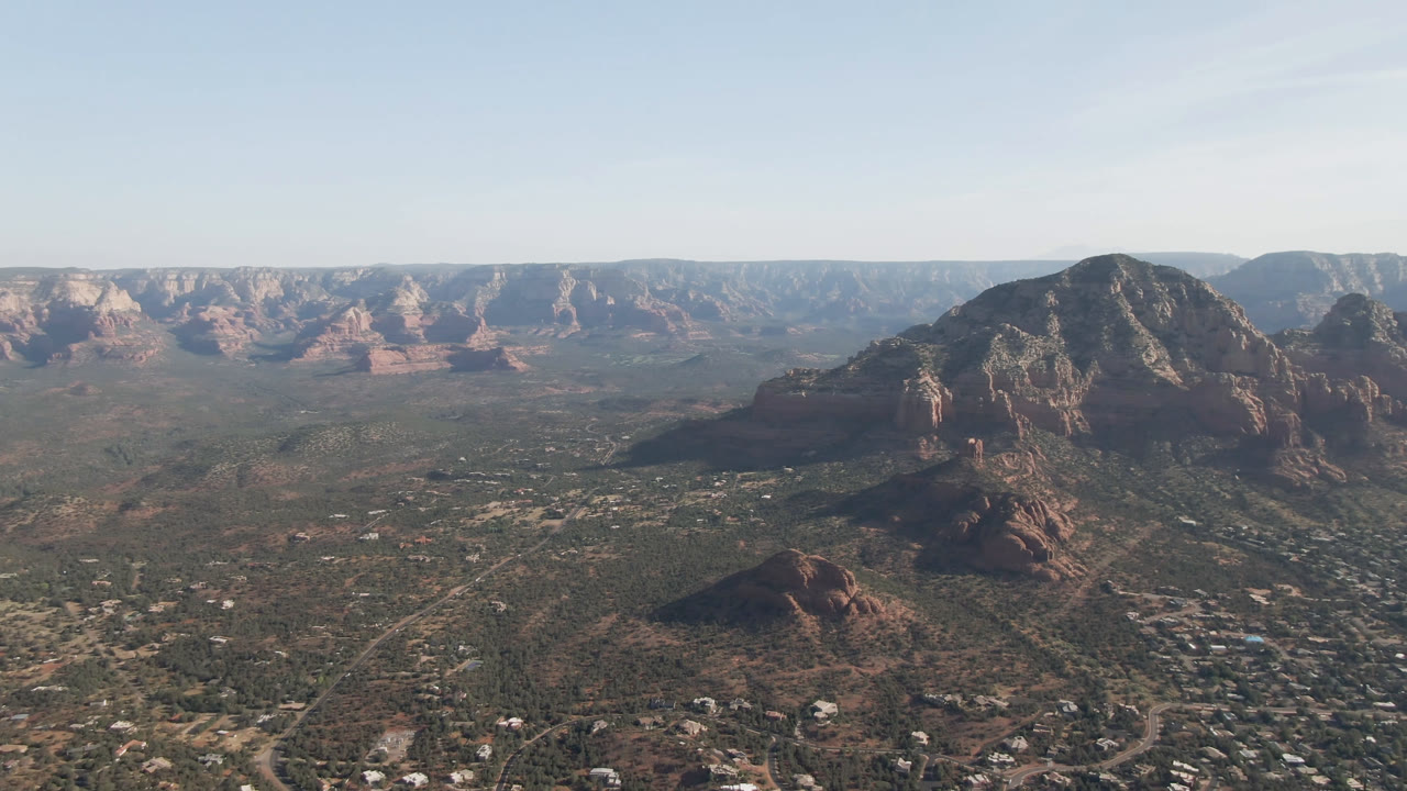Wide drone-like view across a valley toward red mesas and a shadowed mountain.