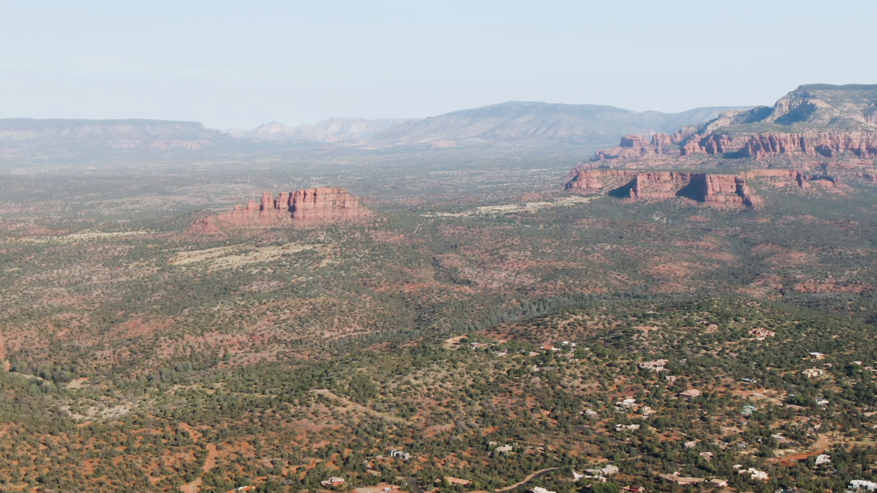 Broad Sedona valley aerial with red rock ridge and mountain backdrop.