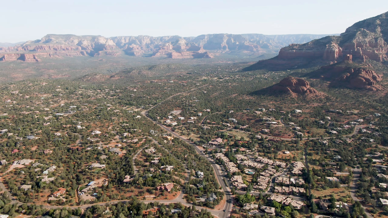 Aerial Sedona view with diagonal road, green valley, and distant red rock ridge