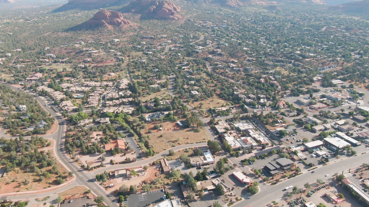Midway across the top row, the Sedona aerial frame shows clustered rooftops, broad roads, sparse desert vegetation, and red rock hills rising behind the town, with no visible people.
