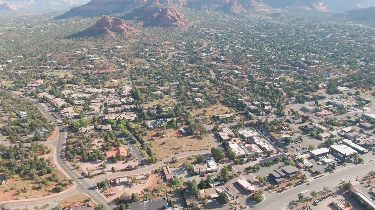 Wide overhead view of Sedona roads, buildings, trees, and red rock formations.