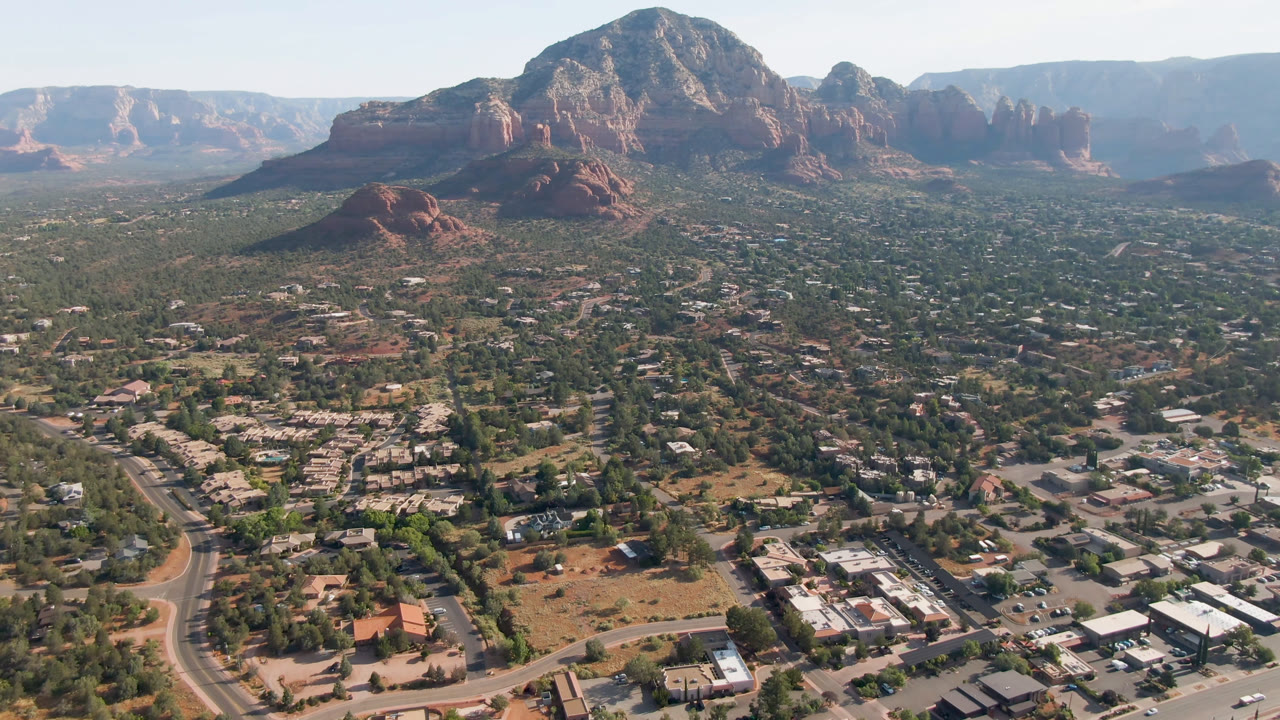 Wide aerial view of Sedona with red rock mountain mass above town streets.
