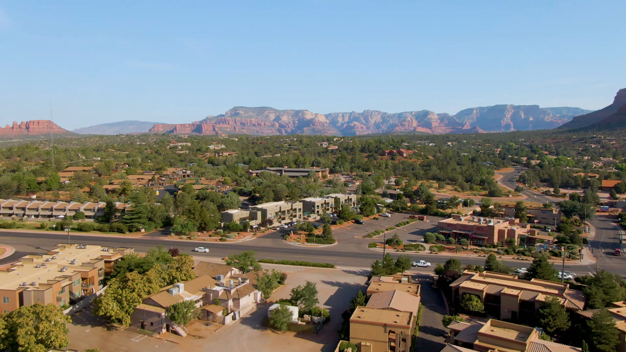 Wide aerial town view with roads, vehicles, trees, and mountains beyond