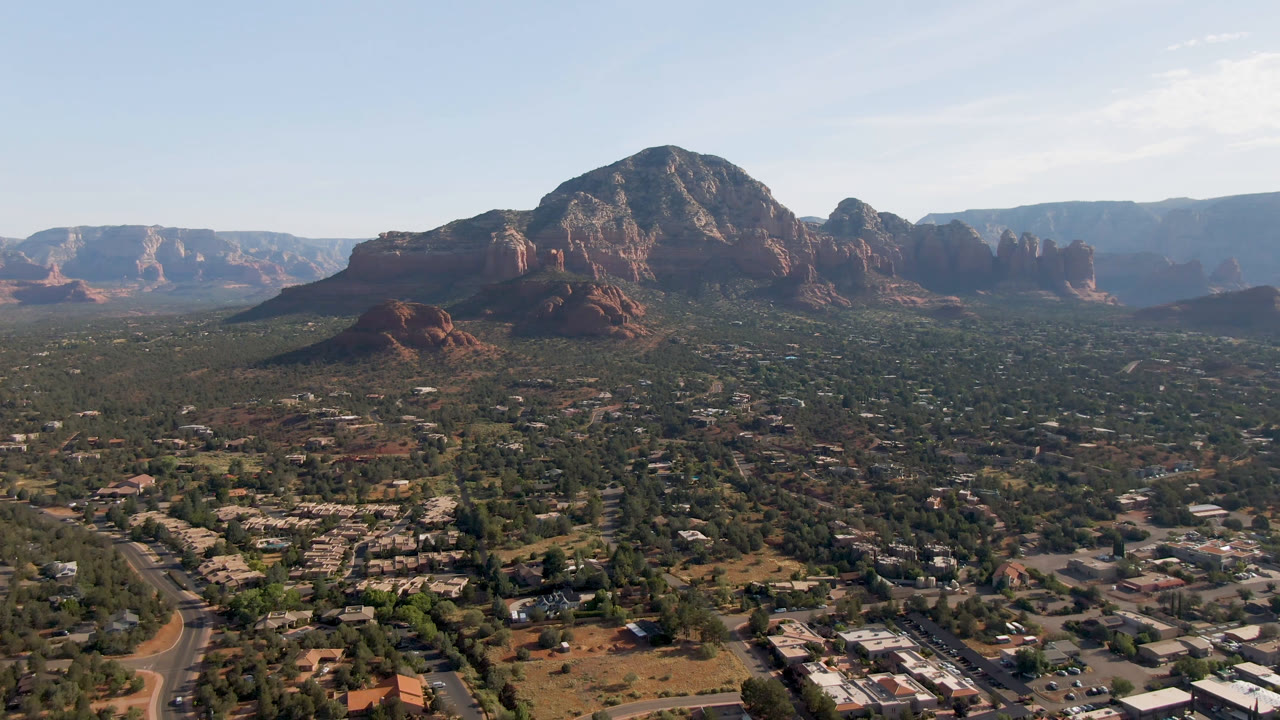 Third frame shows Sedona from above with clustered buildings, curving roads, green desert trees, a central red rock bluff, hazy distant ridges, and no visible people.